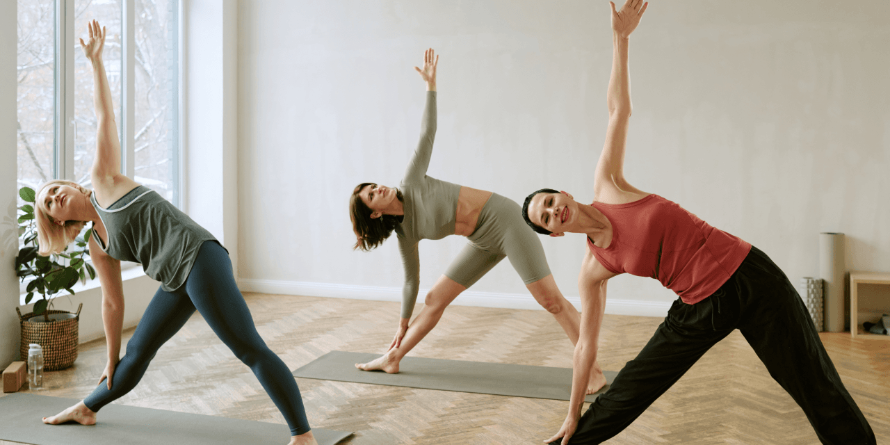 Three women in an airy exercise room doing yoga.