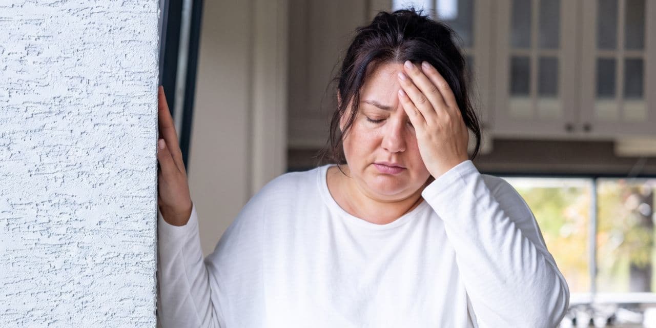Woman feeling dizzy, leaning against a wall for stability