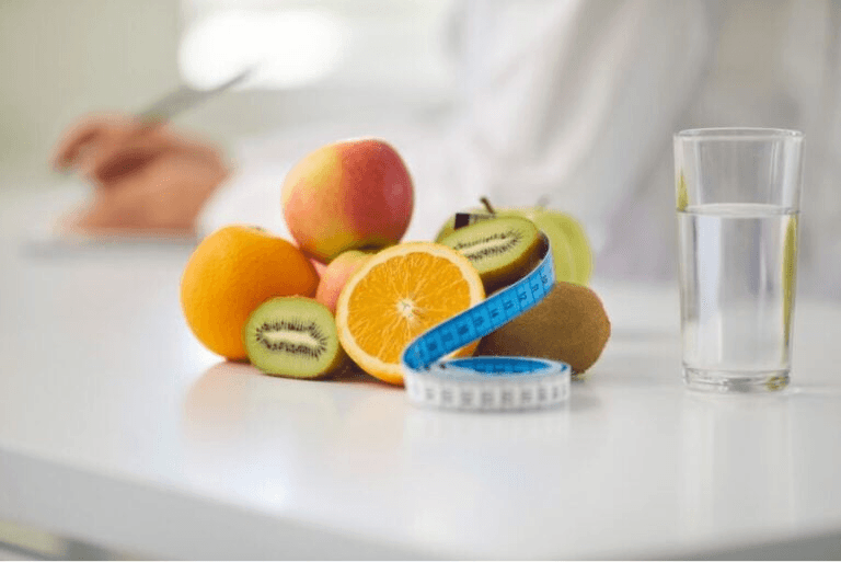 An image showing a glass of water alongside oranges and kiwis, some of the best foods for weight loss.