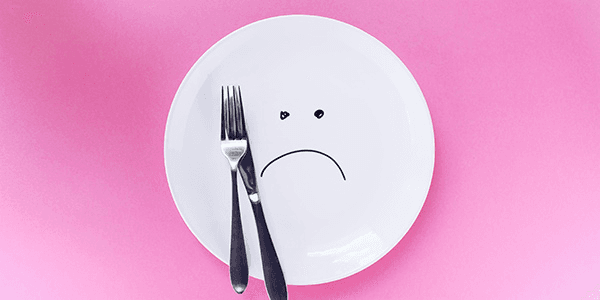An image of a plate with a knife and fork laid on top. There is a sad face on it, indicating that weight loss has become a concern.
