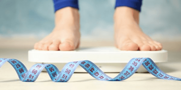 An image of a person on scales with a tape measure in front. They are either taking Orlistat or Saxenda.