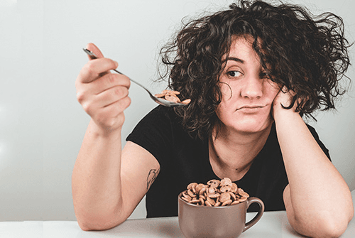 A woman with a bowl of cereal who is emotional eating.