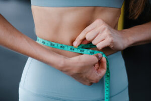 Woman in light blue leggings and a matching crop top measuring her waist with a tape measure
