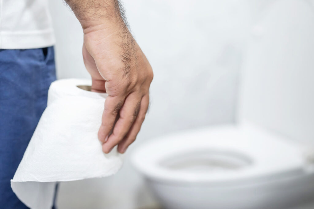 man with a stomachache holding toilet paper in the bathroom